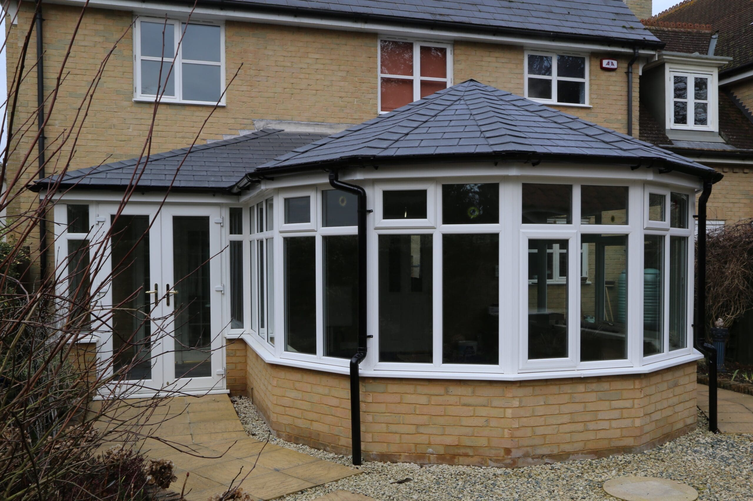 P shape conservatory with a dark solid roof and bay front on a brick house