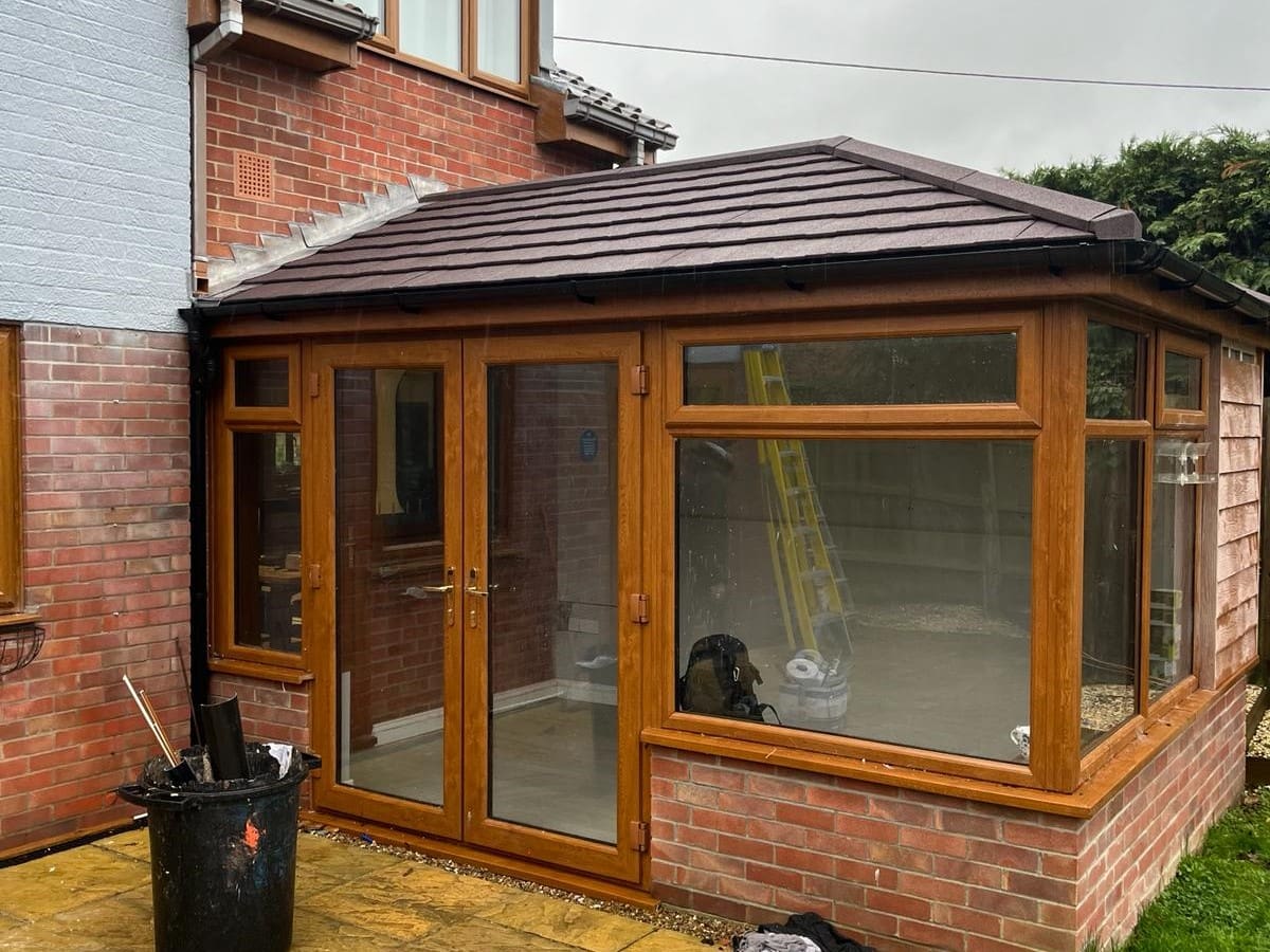 Conservatory with oak effect frames and a dark solid warm roof on a brick base